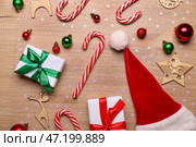 Композиция со сладкими карамельными тростями, шапкой Санты, рождественскими подарками и шарами на деревянном фоне. Стоковое фото, фотограф Pixel_shot / Фотобанк Лори