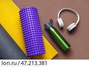 Спортивная бутылка с наушниками, пенопластовый валик и коврик на коричневом фоне. Стоковое фото, фотограф Pixel_shot / Фотобанк Лори