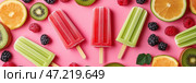 Refreshing summer banner featuring colorful fruit popsicles surrounded by various fruits on a vibrant pink background. На ярко-розовой поверхности разложены яркие мороженые из свежих фруктов, окруженные дольками апельсинов, киви и малины. Веселая летняя атмосфера создается благодаря ярким цветам. Стоковое AI-изображение, AI-художник Katsiaryna Repich / Фотобанк Лори