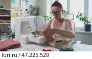 Woman manages home-based sewing business, working on custom orders. Scene shows her multitasking between sewing, managing client requests, and growing her entrepreneurial venture from home. Стоковое видео, видеограф Енваев Андрей / Фотобанк Лори