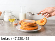 Женщина посыпает сахарной пудрой вкусные тыквенные оладьи на тарелке. Стоковое фото, фотограф Pixel_shot / Фотобанк Лори