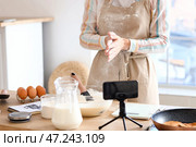 Молодая женщина делает тесто для блинов, следуя видеоуроку на кухне. Стоковое фото, фотограф Pixel_shot / Фотобанк Лори