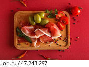 Деревянная доска с вкусным хамоном, оливками, помидорами и специями на цветном фоне. Стоковое фото, фотограф Pixel_shot / Фотобанк Лори