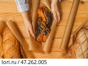 Женщина заворачивает вкусную булочку с маком в бумагу для выпечки на деревянном фоне, вид сверху. Стоковое фото, фотограф Pixel_shot / Фотобанк Лори