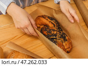 Женщина заворачивает вкусную булочку с маком в бумагу для выпечки за деревянным столом, крупным планом. Стоковое фото, фотограф Pixel_shot / Фотобанк Лори