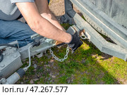 A man attaches a trailer to a car, securing safety chains to the trailer's hitch and drawbar. Стоковое фото, фотограф Коханова Наталья / Фотобанк Лори