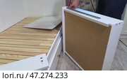 The man is assembling pull-out shelves for the sofa bed. He attaches telescopic slides to the side surfaces of the shelf. Стоковое видео, видеограф Vadzim Yakubovich / Фотобанк Лори