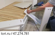 The man is assembling pull-out shelves for the sofa bed from wooden panels. He installs cam lock fasteners. Стоковое видео, видеограф Vadzim Yakubovich / Фотобанк Лори