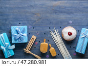 Вкусный пончик с дрейделами, свечами, погремушками и подарками для празднования Хануки на синем деревянном фоне. Стоковое фото, фотограф Pixel_shot / Фотобанк Лори
