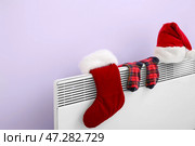 Шапка Санта-Клауса и теплые носки сушатся на электрическом радиаторе возле сиреневой стены, крупным планом. Стоковое фото, фотограф Pixel_shot / Фотобанк Лори