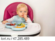 Baby food. The first meal. Feeding the baby. A cute little kid eats vegetables. Healthy food. The child is sitting on a high chair for feeding. Fresh vegetables and fruits. Стоковое фото, фотограф Photojuli / Фотобанк Лори