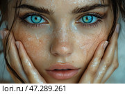 Close-up of a young girl's face with captivatingly bright blue eyes. Her skin is slightly damp, covered with small drops of water, which creates a fresh effect. Freckles, natural skin texture and a light blush are visible. Her lips are slightly parted, and her hands gently touch her face. Her hair is slightly disheveled, with individual strands framing her face. The atmosphere of the photo conveys a sense of natural beauty, liveliness and deep emotionality. Стоковое AI-изображение, AI-художник Анна Кривицкая / Фотобанк Лори