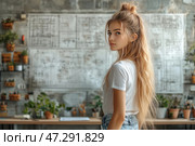 A young girl with long blonde hair stands in a creative workspace. She is dressed in a white T-shirt and jeans, her gaze is directed backwards, creating an effect of slight intrigue. The background includes an industrial style with concrete walls decorated with large drawings, as well as shelves with plants and tools for work. The atmosphere of the photo combines naturalness, creativity and coziness, emphasizing the harmony of industrial and natural elements. Стоковое AI-изображение, AI-художник Анна Кривицкая / Фотобанк Лори