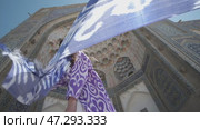A young woman with long hair in an oriental robe and skullcap stands in the wind near an ancient mosque. Стоковое видео, видеограф Aleksey Kidisyuk / Фотобанк Лори