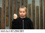 Confident Girl Demonstrating Strength With a Raised Fist in a Creative Indoor Setting. Стоковое фото, фотограф Aleksandr Golubev / Фотобанк Лори