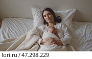 A mother holding her newborn baby, both wrapped in a soft blanket, sitting on a bed in a moment of tender intimacy and warmth. Стоковое AI-видео, аниматор Башкирова Анна / Фотобанк Лори