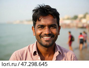 A cheerful man stands near the banks of the Ganges River in Varanasi, reflecting the lively atmosphere. Background figures wander the sandy shore, capturing the essence of local life Generative AI. Стоковое AI-изображение, AI-художник Юлия Петровская / Фотобанк Лори