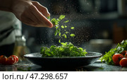A chefs hand sprinkles fresh herbs onto a bowl with colorful salad ingredients. Рука повара сыплет свежую зелень в миску с салатом. Стоковое AI-изображение, AI-художник Katsiaryna Repich / Фотобанк Лори