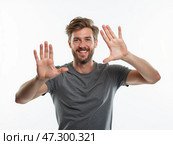 Smiling Man Gestures With Hands in a Welcoming Pose Against a Light Background During Daylight Hours. Стоковое AI-изображение, AI-художник Sergey Grishin / Фотобанк Лори