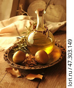 Still life in warm, golden-brown tones. In the center of the composition is a glass bottle of aromatic oil, corked and decorated with rope weaving. It stands on a wooden plate with a carved pattern, next to which lie two ripe fruits (probably olives or dates) and pieces of aromatic resin. Around it are dried leaves and a twig of a plant, giving the picture a natural and rustic simplicity. The atmosphere is warm, cozy, conveying the spirit of traditional village life or an ancient ritual associated with oil and natural gifts. Стоковое AI-изображение, AI-художник Анна Кривицкая / Фотобанк Лори