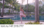 A woman learns to do yoga by the pool at a hotel with palm trees in Thailand in the morning. Her body is shaking, but she tries to do yoga poses correctly. Стоковое видео, видеограф Владимир Разгуляев / Фотобанк Лори