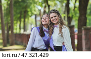 Two girls in graduation sashes embrace in the park on their last day of school. Стоковое фото, фотограф Mikhail Davidovich / Фотобанк Лори
