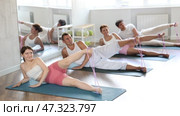 Group of young adults maintaining physical health practicing pilates with elastic band, lying on side and stretching legs at fitness center. Стоковое видео, видеограф Яков Филимонов / Фотобанк Лори
