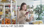 Smiling young girl shopper carefully examining mayonnaise on shelves of food store, scan QR code. Стоковое видео, видеограф Яков Филимонов / Фотобанк Лори
