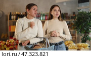 Two female friends buy food and groceries in a supermarket. Young European women talking in the aisle of a grocery store and discussing discounts with promotions. Стоковое видео, видеограф Яков Филимонов / Фотобанк Лори