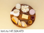 Top view of delicious breakfast with white bread and fresh dairy organic products - cottage cheese, yogurt, butter, milk on wooden plate on light table. Healthy lifestyle. Flat lay, close-up, copy space. Стоковое фото, фотограф Виктория Катьянова / Фотобанк Лори