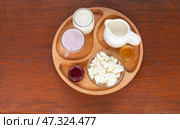 Top view of four types of organic dairy products cottage cheese, yogurt, milk and sour cream on a wooden plate. Tasty and healthy breakfast. Healthy lifestyle. Flat lay, close-up, copy space. Стоковое фото, фотограф Виктория Катьянова / Фотобанк Лори