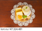 Different types of hard and soft cheeses with basil and walnuts on cutting board on handmade crochet lace napkin on wooden table. Camembert, Caciotta, Parmesan. Top view, flat lay, copy space. Стоковое фото, фотограф Виктория Катьянова / Фотобанк Лори