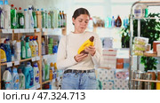 Girl housewife in household store examines and chooses polishing agent for wooden furniture, parquet. Стоковое видео, видеограф Яков Филимонов / Фотобанк Лори