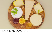 Video of various types of hard and soft cheeses with basil, honey, fruit jam and walnuts on wooden plate on light table. Organic nutritious products. Top view, close-up, flat lay, mock up. Стоковое видео, видеограф Виктория Катьянова / Фотобанк Лори