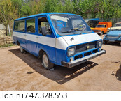 Soviet minibus RAF-2203 "Latvia", painted blue and white. The car has a typical square design of the 70-80s with straight lines and large windows. The front part is equipped with rectangular headlights, a metal bumper and a wide radiator grille. The interior and body look tired - traces of time are visible on the body. The car is parked in an open area, probably a retro-technology museum. Other old cars are visible in the background, including an orange van, a blue convertible and an ambulance van, which creates the feeling of an open-air automotive exhibition. Стоковое фото, фотограф Анна Кривицкая / Фотобанк Лори
