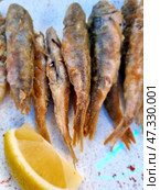 Fried red mullet, neatly piled on a plate. Small golden-brown fish with a crispy crust are a traditional and very aromatic dish, especially popular on the coast. On the side you can see a slice of lemon, which is usually used to give the fish a light citrus freshness. This dish evokes memories of the sea, vacations and warm winds. Стоковое фото, фотограф Анна Кривицкая / Фотобанк Лори