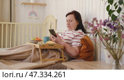 Senior woman having breakfast sitting in bed, drinking tea, enjoying her morning at home. Old lady eating from tray and using phone. Elderly female in pajamas relaxing with cup of coffee in a bedroom. Стоковое видео, видеограф Марина Демидюк / Фотобанк Лори