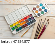 Watercolor paints and brushes arranged on a wooden table ready for an artistic project at a creative workspace during the afternoon. Стоковое AI-изображение, AI-художник Анна Сивакова / Фотобанк Лори