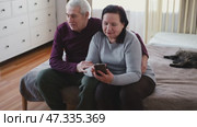 Old couple using a phone together while relaxing in the kitchen at home. Elderly man and woman spending leisure time browsing online with a smartphone. Happy senior married couple typing, learning. Стоковое видео, видеограф Марина Демидюк / Фотобанк Лори