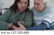 Old couple using a phone together while relaxing in the kitchen at home. Elderly man and woman spending leisure time browsing online with a smartphone. Happy senior married couple typing, learning. Стоковое видео, видеограф Марина Демидюк / Фотобанк Лори