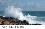 Powerful waves surge against rugged rocks, creating a stunning display of water and spray beneath a bright blue sky on a sunny day by the ocean. Стоковое AI-изображение, AI-художник Sergey Grishin / Фотобанк Лори