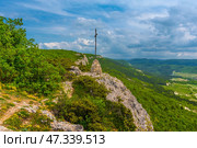 Picturesque landscape in the Chelter-Marmara area (Crimea), one of the most interesting and atmospheric places in the foothills of the Bakhchisaray region. This place is known for its ancient cave monastery, located in the rocks above the valley, surrounded by dense forests. From here, magnificent views of the surrounding mountain ranges covered with greenery open up, and in the distance you can see the hills and the southern coastal expanses. The paths to Chelter lead through forests covered with oaks, pines and shrubs, and are often accompanied by views of steep cliffs, vineyards and pastures.This is a place not only of natural beauty, but also of spiritual peace, here you can feel the breath of history, silence and peace. Стоковое фото, фотограф Анна Кривицкая / Фотобанк Лори