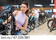 Young woman selects bicycle in sporting goods store, checking wheel quality. Стоковое фото, фотограф Яков Филимонов / Фотобанк Лори