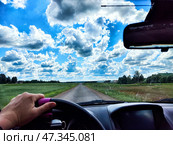 A hand grips the steering wheel as the car moves along a beautiful road under a vast blue sky filled with clouds. Стоковое фото, фотограф Кривошеина Елена Леонидовна / Фотобанк Лори