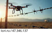 A drone hovers near a barbed wire fence in a barren desert area, capturing the warm glow of sunset and distant mountain silhouettes. Стоковое AI-изображение, AI-художник Sergey Grishin / Фотобанк Лори