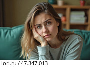 Заботливая молодая женщина, выглядящая напряженной, сидя на диване в уютной гостиной. Стоковое AI-изображение, AI-художник Елена Болотина / Фотобанк Лори