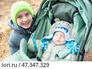 12-летний мальчик рядом со своим младшим братом-младенцем, который спит в зеленой коляске. в весеннем парке. фокус на подростке. Стоковое фото, фотограф Яна Проничева / Фотобанк Лори
