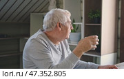 Happy senior man having a coffee break and thinking at home. Face of an old man feeling nostalgic, drink tea during retirement. Elderly man thinking, decision with wellness and calm. Morning routine. Стоковое видео, видеограф Марина Демидюк / Фотобанк Лори