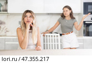 Middle-aged woman sitting at the table while a girl is disputing with her standing behind. Стоковое фото, фотограф Яков Филимонов / Фотобанк Лори