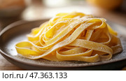 Golden strands of freshly made fettuccine pasta on a matte ceramic plate. Золотистые нити свежеприготовленной пасты феттучине, деликатно сложенные на матовой керамической тарелке. Мягкое теплое освещение подчеркивает текстуру ручной работы на нейтральном фоне, навевая мысли о ремесленном мастерстве. Гиперреалистичный, чистый минимализм. Стоковое AI-изображение, AI-художник Katsiaryna Repich / Фотобанк Лори